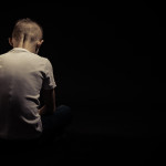 Rear View of a Sad Silhouette Young Boy Sitting on the Floor Against Black Background with Copy Space.